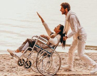 man pushing woman in wheelchair on beach
