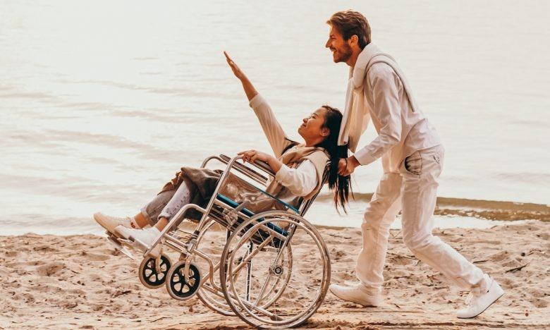 man pushing woman in wheelchair on beach