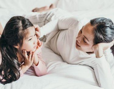 mother talking to young daughter while both lay on bed