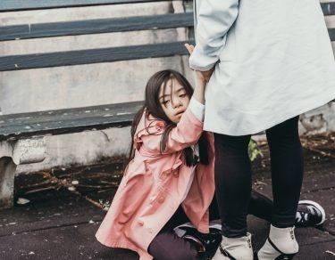 mother holds daughters hands while daughter sits on floor