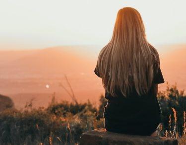 young woman sitting on rock watching sunset