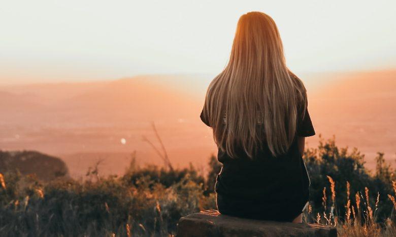 young woman sitting on rock watching sunset