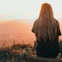 young woman sitting on rock watching sunset