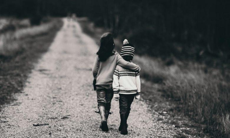 black and white photo of boys hugging while walking on dirt road