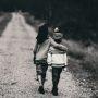 black and white photo of boys hugging while walking on dirt road