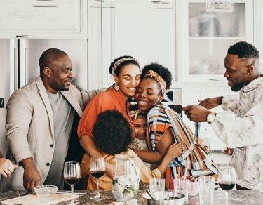 family gathered in kitchen while two women hug