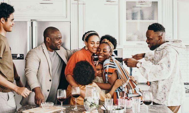family gathered in kitchen while two women hug