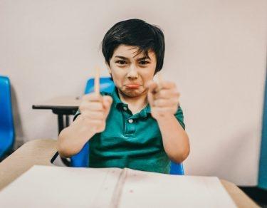 angry boy in classroom breaks pencil in half