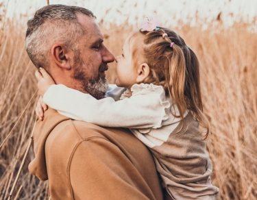 dad looks lovingly at toddler daughter while holding her in wheat field