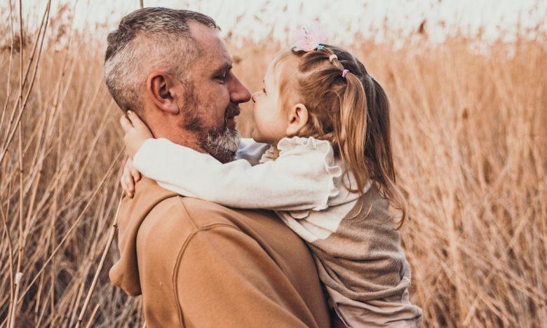 dad looks lovingly at toddler daughter while holding her in wheat field