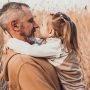 dad looks lovingly at toddler daughter while holding her in wheat field