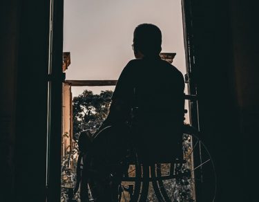 man in wheelchair looks out doors from dark room