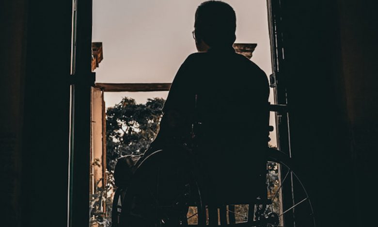 man in wheelchair looks out doors from dark room