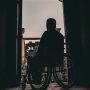 man in wheelchair looks out doors from dark room