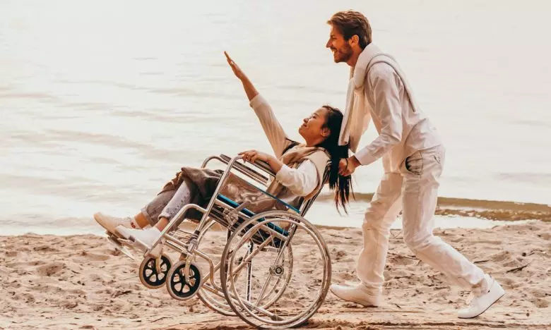man pushing woman in wheelchair on beach