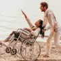 man pushing woman in wheelchair on beach