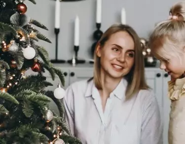 mother and toddler daughter sitting in front of christmas tree