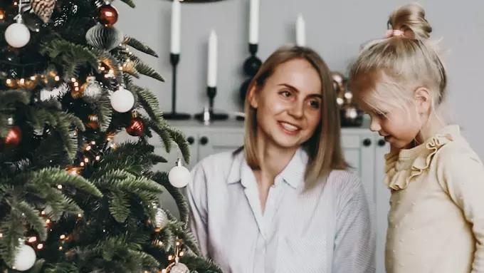 mother and toddler daughter sitting in front of christmas tree