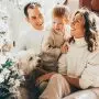 family of 3 sitting in front of christmas tree