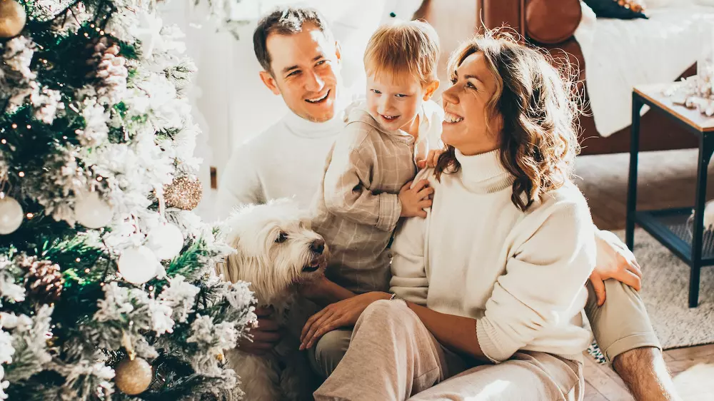 family of 3 sitting in front of christmas tree