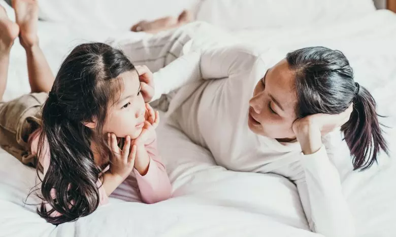 mother talking to young daughter while both lay on bed