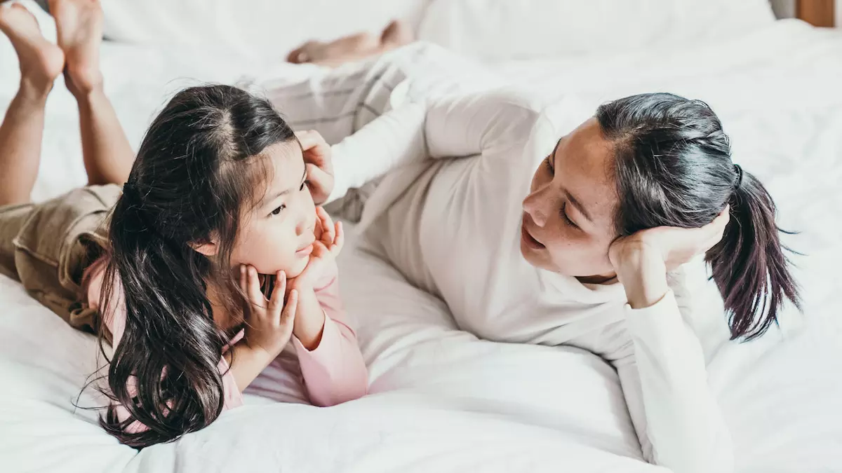 mother talking to young daughter while both lay on bed