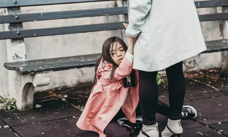 mother holds daughters hands while daughter sits on floor