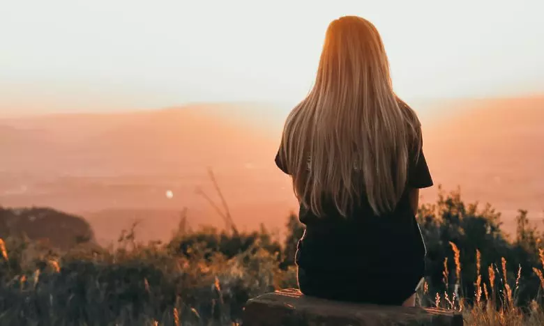 young woman sitting on rock watching sunset