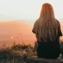 young woman sitting on rock watching sunset