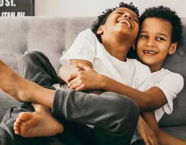 brother wraps legs around sibling while they both laugh