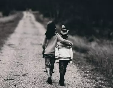 black and white photo of boys hugging while walking on dirt road