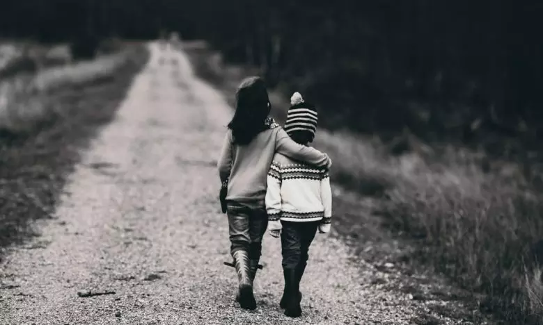black and white photo of boys hugging while walking on dirt road