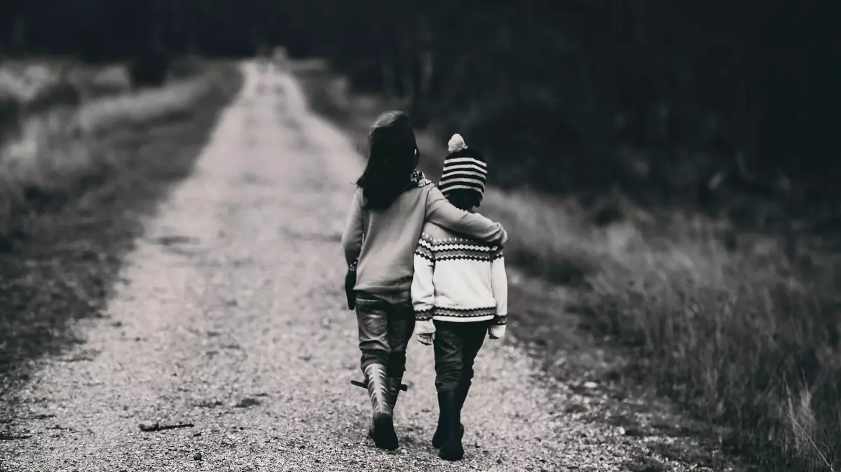 black and white photo of boys hugging while walking on dirt road