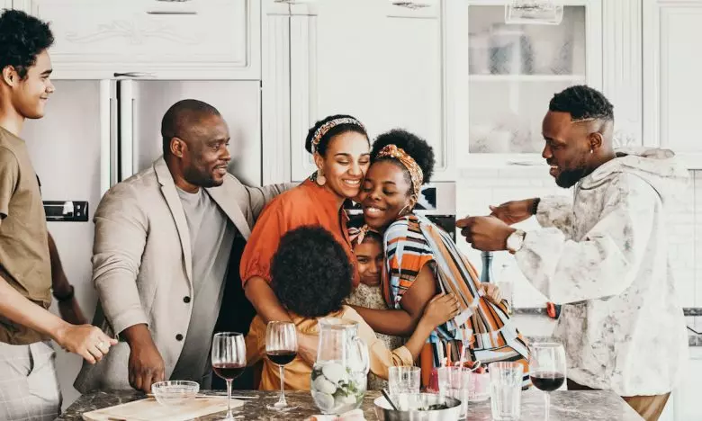 family gathered in kitchen while two women hug