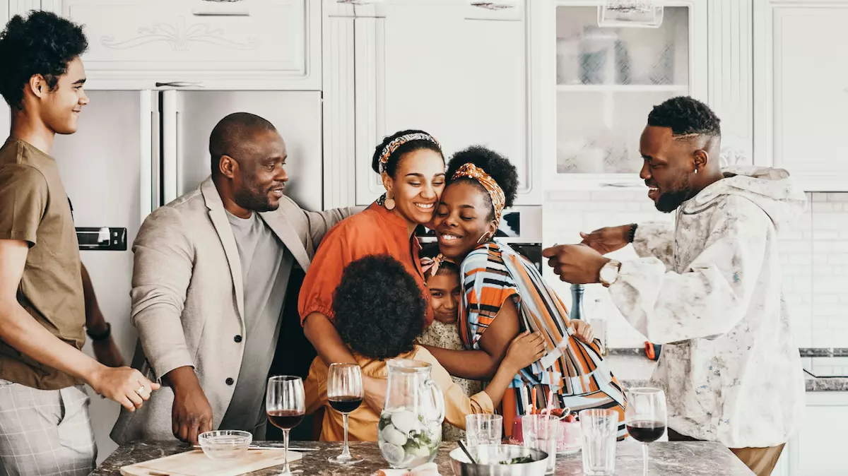 family gathered in kitchen while two women hug