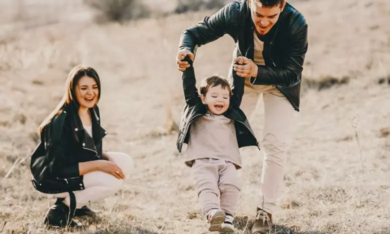 dad throws toddler while holding hands as mom watches and laughs