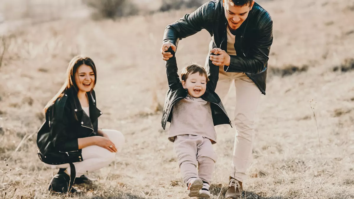 dad throws toddler while holding hands as mom watches and laughs