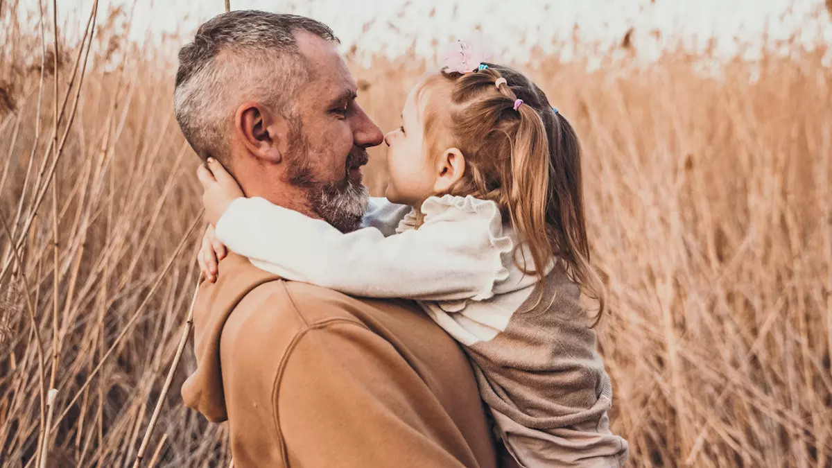 dad looks lovingly at toddler daughter while holding her in wheat field